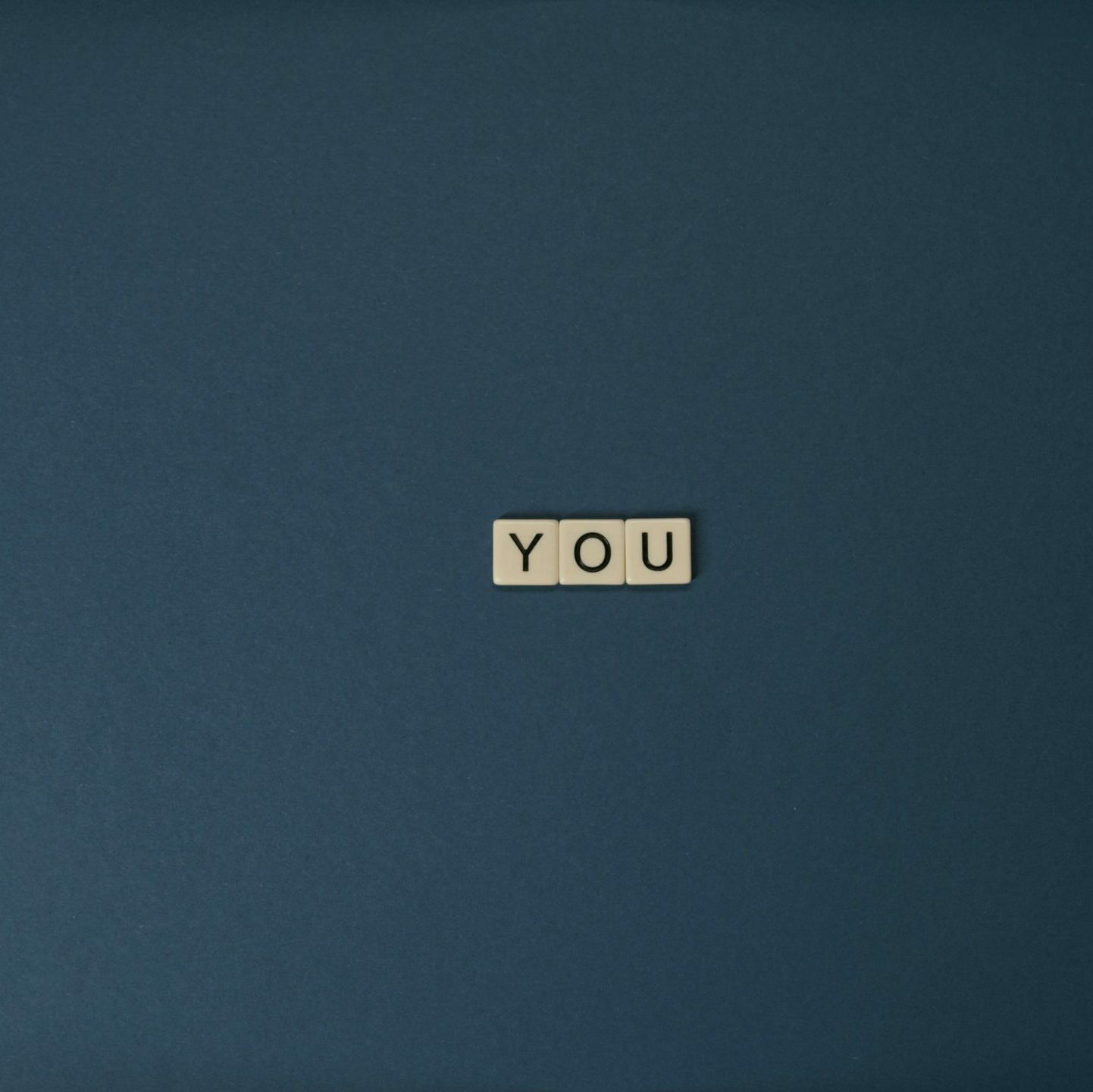 Flat lay of Scrabble letters spelling 'YOU' on a blue background, perfect for conceptual themes.